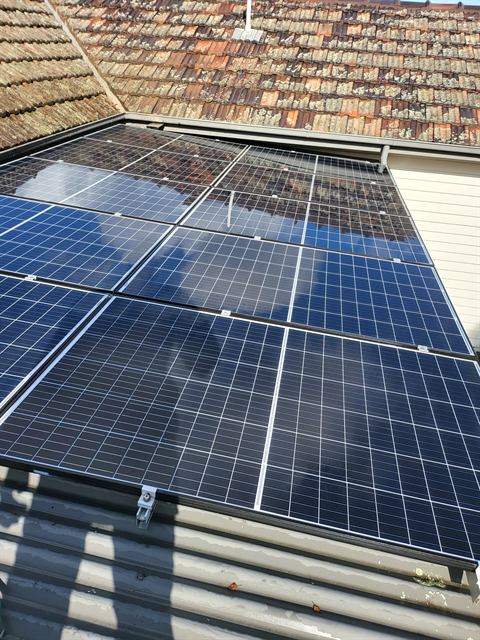 Solar panels on a corrugated roof with a tiled roofline behind