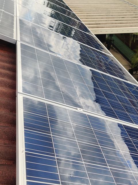 Solar panels along a roof edge with a clear sky reflection